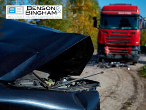 Close-up of a damaged blue car hood in the foreground with a red truck visible in the background, suggesting a truck accident scene in Nevada