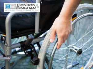 A person's hand is shown gripping the wheel of a manual wheelchair, symbolizing the physical challenges and pain that can follow a car accident