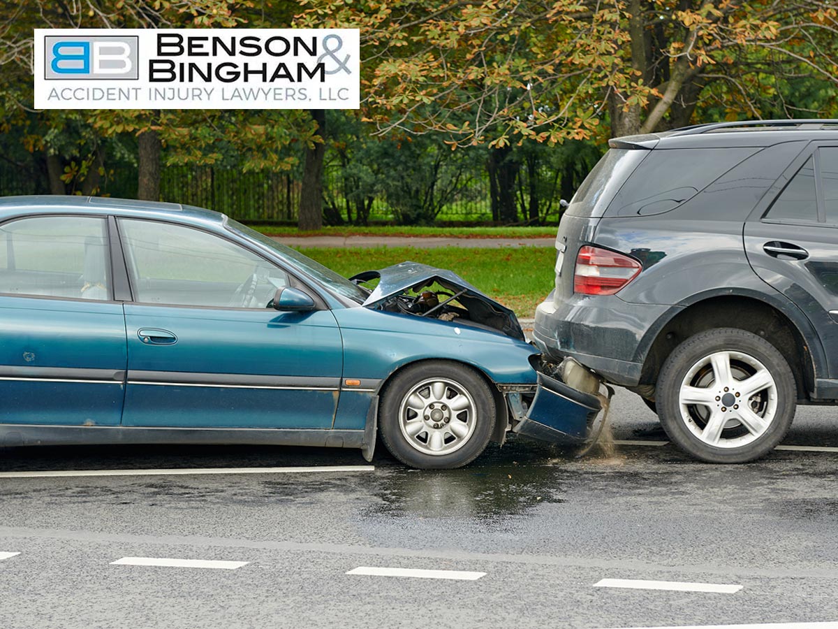 Two cars involved in a rear-end accident with the rear car's front damaged and the lead car's back crushed, on a wet road