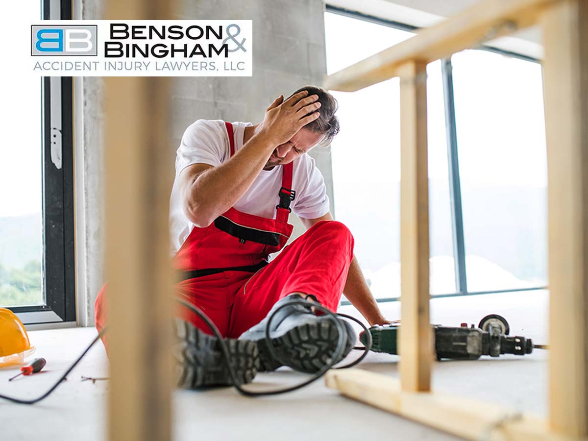 A construction worker in red overalls sitting on the floor with a hand on his head, possibly injured on the job, a situation that could involve Workers' Compensation