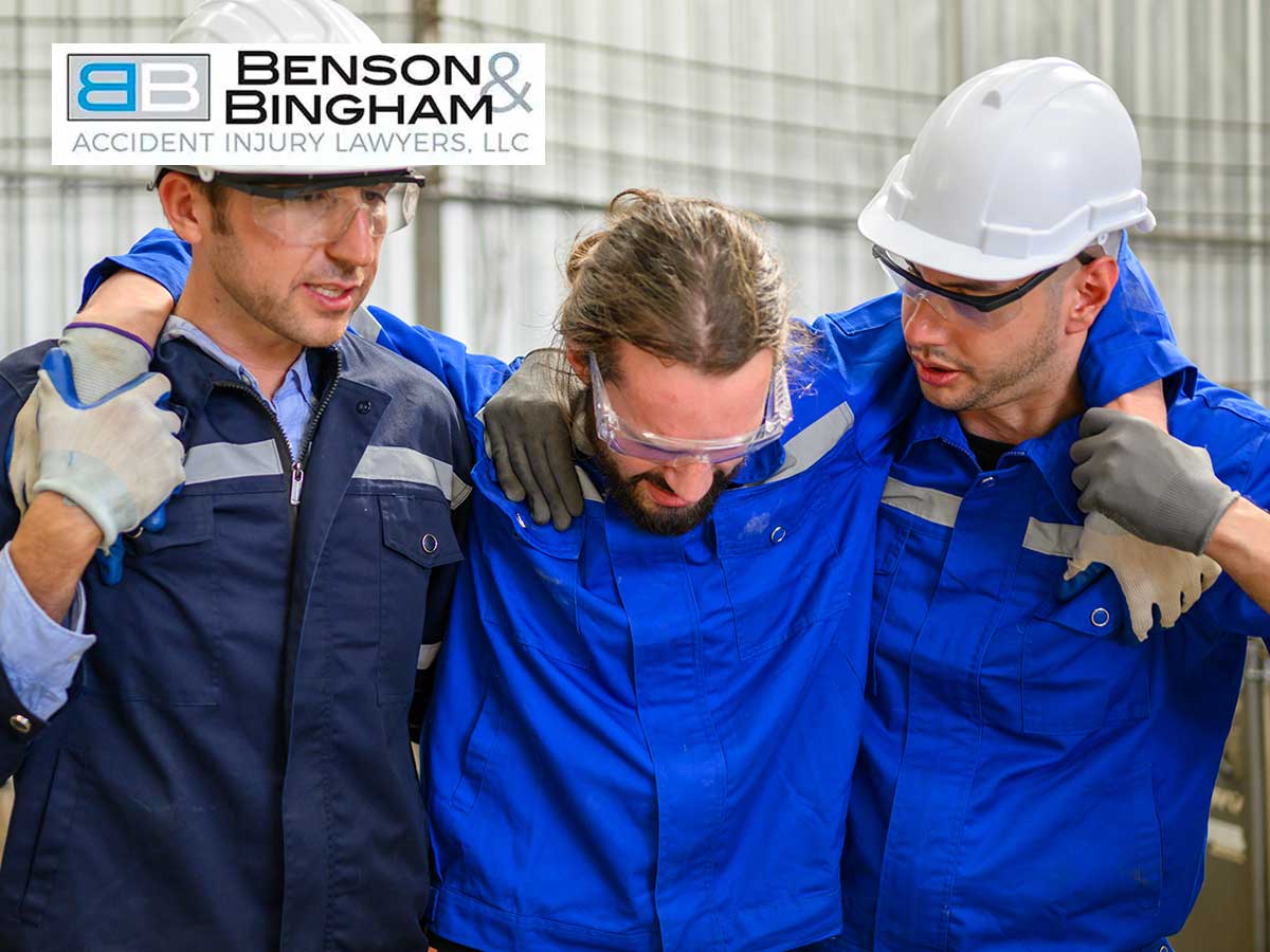 Two workers in blue uniforms and safety helmets supporting an injured colleague, indicating a scenario that may require Workers' Compensation